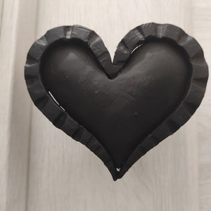 Könnte beinhalten: Ein schwarzer, herzförmiger Metallobjekt mit einem dekorativen, gewellten Rand.