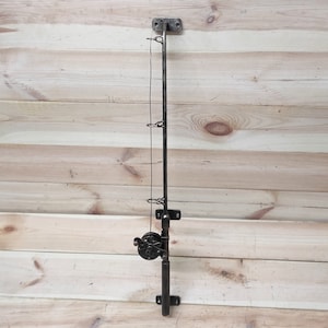 May include: A black metal fishing rod wall mount with a reel and hooks. The mount is attached to a wooden wall.