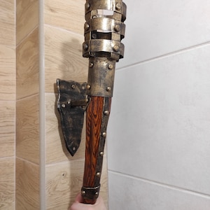 May include: A wall-mounted, decorative torch with a wooden handle and a metal head. The head is made of multiple metal bands with rivets and has a gold finish.