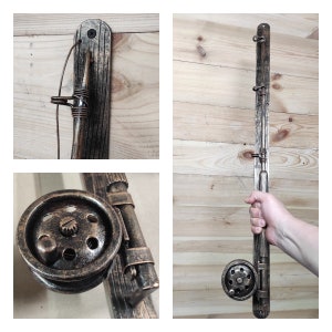 May include: A rustic metal fishing rod wall mount with a faux wood finish. The mount features a metal fishing reel and a hook for hanging fishing rods.