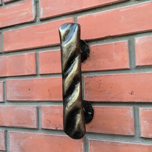 May include: A black and gold metal door handle with a twisted design. The handle is mounted on a brick wall.