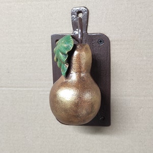 May include: A gold pear-shaped door knocker with a green leaf attached to a brown metal plaque.