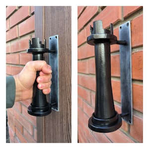 Può includere: Maniglia per porta in metallo nero con un design unico. La maniglia è fissata a una piastra rettangolare in metallo. La maniglia ha la forma di una torre con una cima arrotondata.