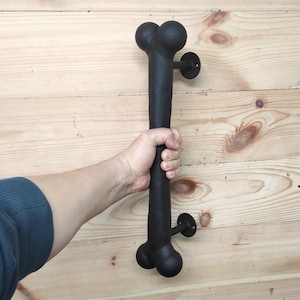 May include: Black bone-shaped door handle with a smooth, matte finish. The handle is held by a hand against a light wood background.