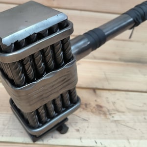 May include: A robust metal hammer with a square head and a handle wrapped in black material. The hammer head is made with multiple rebar rods, and the handle is steel. The hammer is designed for heavy-duty use. The overall design suggests a tool for construction or demolition.