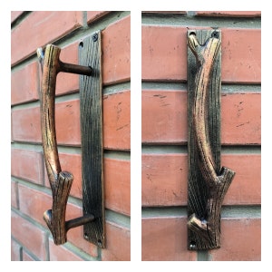 May include: Two rustic, metal door handles with a branch-like design. The handles are mounted on a brick wall and have a dark brown finish with gold accents.