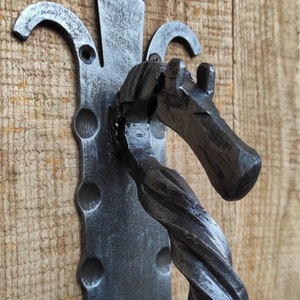 Puede incluir: Un llamador de puerta de metal negro con forma de cabeza de caballo. El llamador está fijado a una puerta de madera.