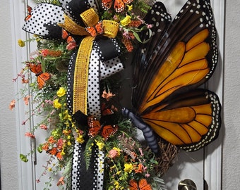 May include: A black and white polka dot bow with a yellow ribbon and a large orange and black butterfly on a green wreath with flowers.