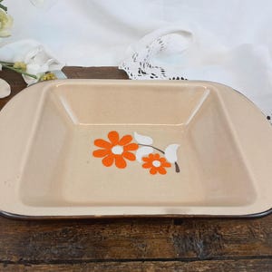 May include: A beige ceramic baking dish with a brown rim and a floral design featuring orange flowers and white leaves.