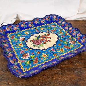 Könnte beinhalten: Ein blaues und weißes Keramik-Serviertablett mit einem gewellten Rand. Das Tablett ist mit einem floralen Muster in den Farben Rosa, Gelb, Grün und Rot verziert.