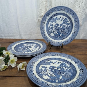 Op de afbeelding: Een set blauw-witte keramische borden met een klassiek Willow-patroon. De borden tonen een gedetailleerd landschapsontwerp met pagodes en figuren. De borden zijn gerangschikt op een houten oppervlak.