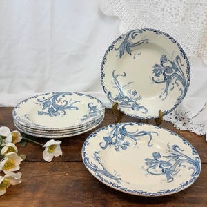May include: Set of six white ceramic soup bowls with a blue and white floral pattern. The bowls have a scalloped edge and are stacked on top of each other.