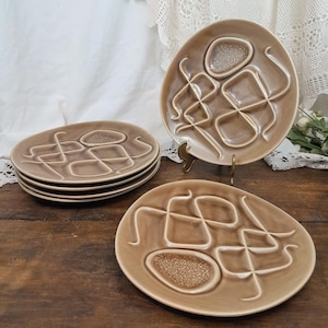 May include: Set of six brown ceramic plates with a raised geometric design. The plates have a textured surface and a slightly oval shape.