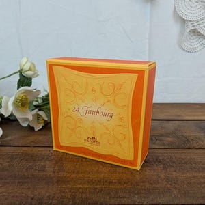 Peut inclure: Une boîte orange de parfum 24 Faubourg Eau de Toilette. La boîte a une étiquette jaune avec le nom du parfum et le logo Hermès. La boîte est de 47 ml.