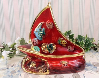 Può includere: Piatto portaoggetti in ceramica rossa a forma di barca a vela con dettagli dorati e disegni colorati di pesci e coralli.