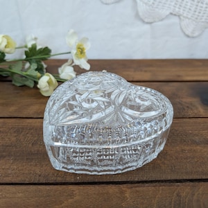May include: A clear, heart-shaped trinket box with a cut-glass design. The box is made of crystal and sits on a wooden surface. The lid features a floral pattern. The box is approximately 10 cm wide.