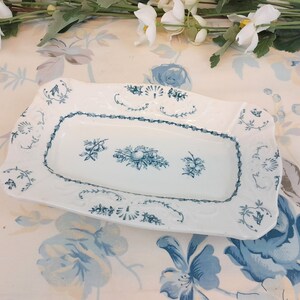 May include: A white rectangular serving dish with a blue floral design. The dish has a raised rim and a scalloped edge.