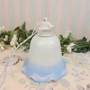 Peut inclure: Un abat-jour de lampe en verre blanc et bleu avec un bord festonné. L'abat-jour est suspendu à un support de cordon en céramique blanche.