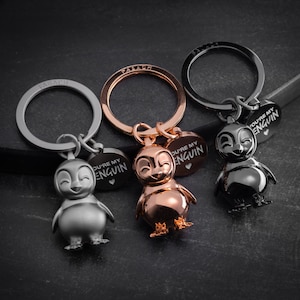 Könnte beinhalten: Drei silberne Schlüsselanhänger mit Pinguin-Anhängern. Jeder Anhänger hat ein herzförmiges Schild mit der Aufschrift "You're my penguin".