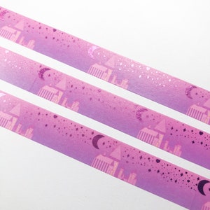 May include: Three rolls of pink washi tape with a holographic finish. The tape features a repeating pattern of a crescent moon, stars, and a pink building with windows.