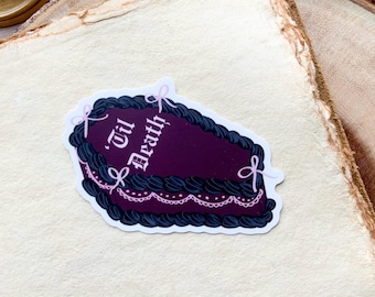 May include: A sticker of a dark purple coffin-shaped cake with black frosting and pink bows. The cake is decorated with white lace and the text "Til Death" in white.