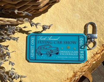 May include: A blue ticket with the text "Sixth Annual Flying Car Show" and a cartoon image of a flying car. The ticket also says "Omnioculars Encouraged" and "Also available for purchase".
