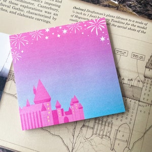 May include: A pink and blue sticky note with a white outline of a castle and fireworks. The sticky note is on top of a page with a black and white drawing of a castle.