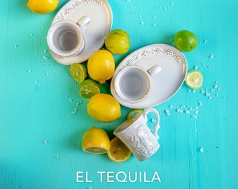 Puede incluir: Dos tazas de cerámica blanca con asas sobre platos blancos con diseños florales. Las tazas están llenas de un líquido transparente. Los platos están rodeados de limones y limas sobre un fondo turquesa. El texto "EL TEQUILA" está en la parte inferior de la imagen.
