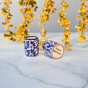 May include: Two blue and white ceramic shot glasses with a floral pattern. One glass has the words "Dulce Nostalgia" written on it.