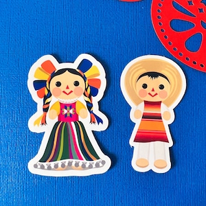 May include: Two colourful Mexican folk art dolls, a girl with a long colourful skirt and a boy wearing a straw hat and a striped shirt.