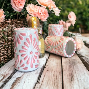 Könnte beinhalten: Vier weiße Keramikschnapsgläser mit rosafarbenen Blumendesigns. Die Gläser stehen auf einer Holzoberfläche mit einem verschwommenen Hintergrund aus rosa Blumen.