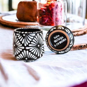 May include: Two black ceramic cups with white floral designs. One cup has the text "Dulce Nostalgia" and "H.EN MEXICO" written on the bottom.