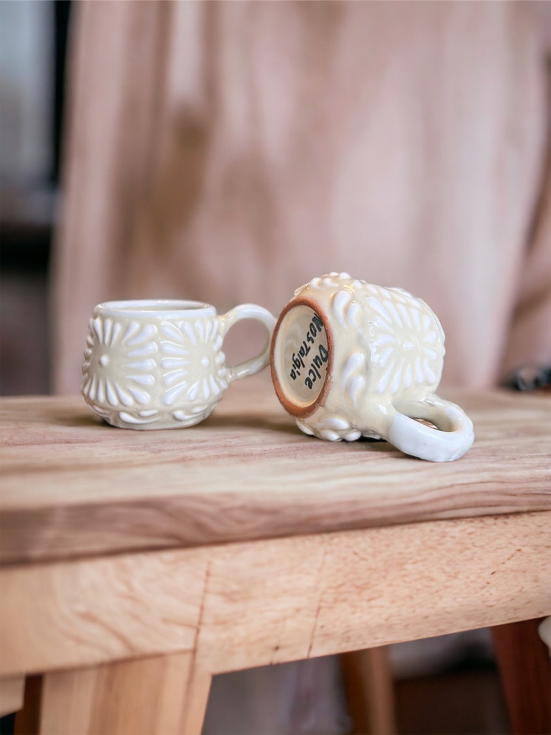 May include: Two white ceramic mugs with a raised floral design. One mug has the words "Juice  Nostalgia" written on it.