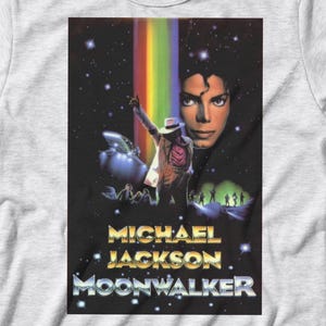 May include: A light gray t-shirt featuring a graphic from the movie "Moonwalker." The graphic includes an image of Michael Jackson, a rainbow, and the movie title. The shirt is a crew neck and has short sleeves.