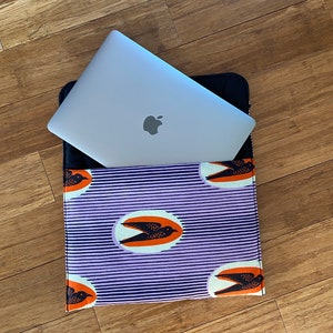 Peut inclure: Une housse pour ordinateur portable de couleur violette et noire avec un fond blanc et un motif de cercles orange avec des oiseaux noirs volant à l'intérieur. La housse est posée à plat avec un ordinateur portable argenté à l'intérieur.