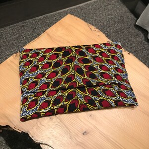 Peut inclure: Une pochette en tissu à motif jaune, rouge et bleu. Le tissu présente un motif géométrique avec un motif répétitif de feuilles rouges et jaunes.