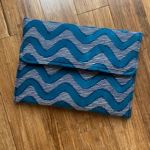 Op de afbeelding: Een tealblauwe en witte stoffen clutch met een patroon en een klep.