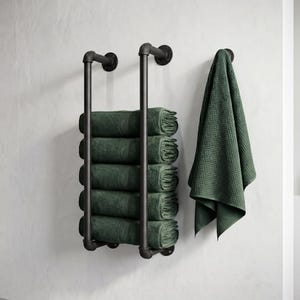 Könnte beinhalten: Ein schwarzer Metall-Handtuchhalter mit sechs gefalteten grünen Handtüchern. Ein grünes Waffel-Handtuch hängt an einem Haken. Der Halter ist an einer weißen Wand montiert, was auf ein Badezimmer hindeutet.