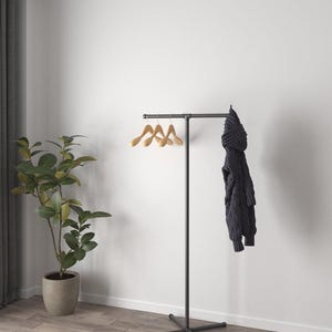 May include: A black metal clothes rack with a cross base. Three wooden coat hangers are on the top bar. A dark blue jumper hangs on the right side. A potted plant is on the left.