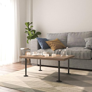 May include: A rectangular wooden coffee table with black metal legs. The table is in a living room setting, with a gray sofa, decorative pillows, and a rug. The table has a light brown finish and is approximately 48 inches long.