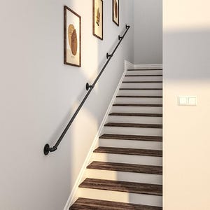 Könnte beinhalten: Ein schwarzer Metallhandlauf an einer weißen Wand neben einer Holztreppe. Drei gerahmte abstrakte Kunstwerke hängen an der Wand. Die Treppe hat braune Holzstufen und weiße Setzstufen.