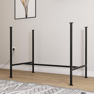 May include: Black metal table frame with four vertical legs and a horizontal support structure. The frame is designed for a table and is set against a neutral wall with a framed artwork. The legs are square and the frame is on a wooden floor.