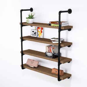 May include: A four-tier wall-mounted shelf unit with a rustic design. The shelves are made of brown wood and supported by black metal pipes. The shelves hold books, a plant, artwork, and a purse.