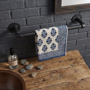 May include: A black metal towel rail fixed to a dark grey brick wall. A patterned blue and white towel hangs from the rail. A clear glass bottle with a black pump and some stones are on a wooden surface.