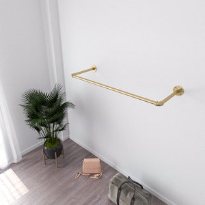 Modern minimalist interior with a golden wall-mounted clothes rack holding a beige sweater and two wooden hangers.