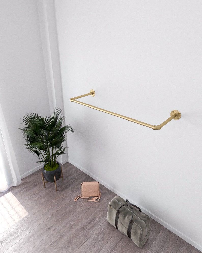 Modern minimalist interior with a golden wall-mounted clothes rack holding a beige sweater and two wooden hangers.