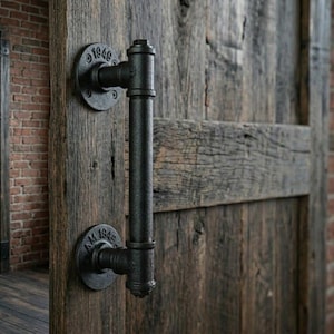 Puede incluir: Manija de puerta negra de estilo industrial hecha de tuberías y accesorios, montada en una puerta de madera envejecida. La manija tiene una barra vertical y dos placas de montaje circulares, cada una con el año "1949" en relieve. La puerta es de madera recuperada.