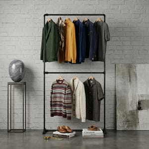 Puede incluir: Un perchero de metal negro que exhibe varias prendas, incluyendo una blazer verde, un cuello alto amarillo y una chaqueta vaquera. Debajo, un suéter estampado, una rebeca crema y una camisa de manga corta. Accesorios: zapatos, libros y cinturón.