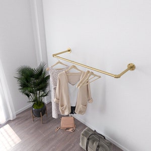 Modern minimalist interior with a golden wall-mounted clothes rack holding a beige sweater and two wooden hangers.