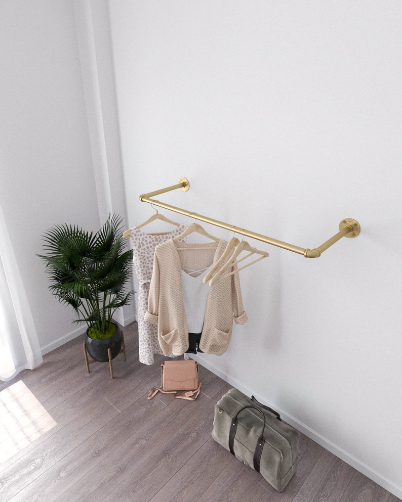 Modern minimalist interior with a golden wall-mounted clothes rack holding a beige sweater and two wooden hangers.